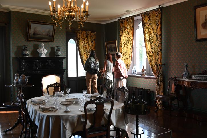 Salle à manger du château avec la table dressée à l'anglaise et la française, au fond trois personnes observent les décors